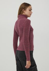 Maglione a collo alto a costine rosa con un design aderente e maniche lunghe. Tessuto morbido, con un alto collo, indossato con pantaloni cargo scuri.