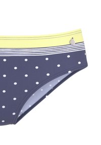 Bas de bikini bleu marine avec des pois blancs, avec une bande jaune à la taille. Comprend un accent logo en argent. Texture lisse.