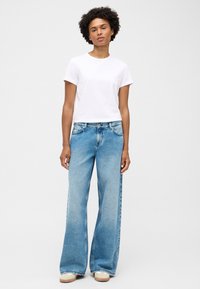 Biała koszulka z okrągłym dekoltem zestawiona z szerokimi, jasnoniebieskimi dżinsami. Dżinsy mają wyblakły kolor, pięć kieszeni i lekko strzępiony dół.