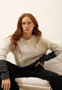 Sweter dzianinowy o jasnobeżowym korpusie z ciemnoszarym dołem i mankietami. Teksturowany materiał z okrągłym dekoltem i luźnym krojem. Czarne spodnie.