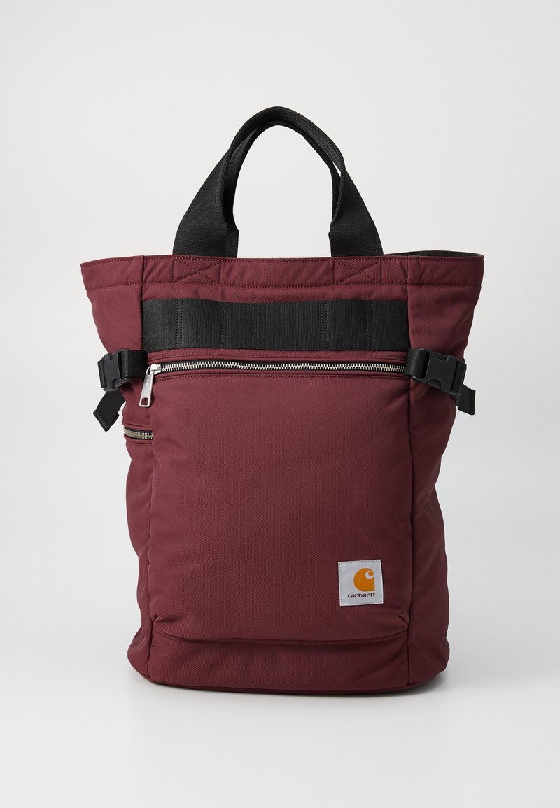 Burgunderfarget stoff tote bag med svarte stropper, med en frontlomme med glidelås og sideknepping. Inkluderer en liten logo i det nedre hjørnet.