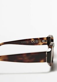 Kocourovy sluneční brýle s širokým čtvercovým rámem. Disponují vyrytými značkami CE a UKCA na vnitřním rameni, kategorie N, lesklý povrch.