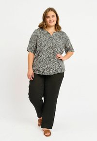 Blusa a righe bianco e nero con maniche corte e scollo a V, abbinata a pantaloni neri larghi e sandali scivolati marroni.