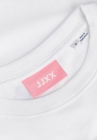 Λευκό T-shirt με στρογγυλή λαιμόκοψη με ροζ ετικέτα της μάρκας JJXX και ετικέτα μεγέθους S, κατασκευασμένο στο Μπαγκλαντές, ορατό μέσα στο γιακά.