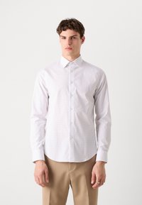 Hvit skjorte med små prikkemønster, lange ermer og klassisk krage, brukt sammen med beige bukser. Glatt tekstur.