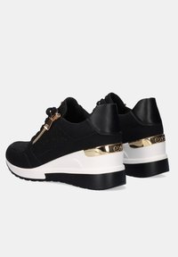Zapatillas negras con parte superior de tejido texturizado y acentos de cuero suave. Presenta un acento de talón metálico dorado y suela de plataforma blanca.