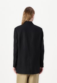 Blazer noir ajusté avec col en V, manches longues et poignets boutonnés. Tissu lisse avec une coupe droite et un détail d'ouverture au dos.