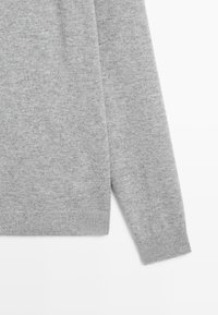 Light grey knitted sweater with a soft texture, featuring a round neckline and ribbed cuffs. Overall simple design without patterns or accents.