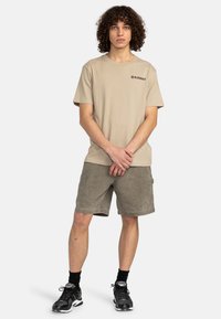 Beige bavlnené tričko s logom Element, v kombinácii so zelene olivovými kordovými šortkami. Model má na sebe čierne tenisky a ponožky do polovice lýtok.