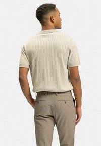 Benvit randig polo-shirt med korta ärmar, bärs med ljusa bruna byxor som har bakfickor och knappdetaljer.