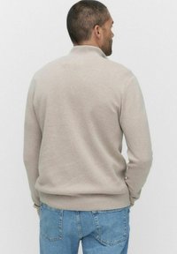 Ljusbeige sweatshirt med hög krage, ribbade manschetter och nederkant, med en mjuk textur och avslappnad passform, bärs med blå jeans.