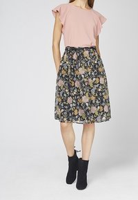 Roze top met gerimpelde mouwen, gecombineerd met een zwarte rok met bloemenpatroon in verschillende kleuren. De look wordt afgemaakt met zwarte enkelboots.
