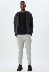 Svart zip-up jacka med huva, kombinerad med svart t-shirt och ljusgrå sweatpants. Svarta sneakers fulländar outfiten.
