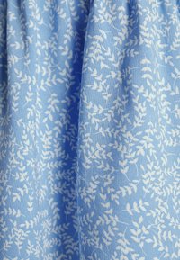 Tessuto blu con un motivo a foglie bianche, caratterizzato da una texture morbida e una qualità fluida. Il design è ripetuto su tutta la superficie del materiale.