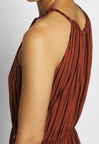 Hnědé šaty bez rukávů s černými vertikálními pruhy, s nařaseným výstřihem a vypasovaným pasem s knoflíkovým detailem na boku.