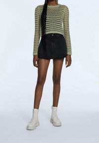 Maglione lavorato a maglia di colore verde chiaro con una grande trama aperta, abbinato a una mini gonna in denim nera e stivali da combattimento color crema.