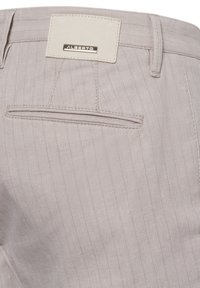 Helle beige gestreifte Hose mit glatter Textur. Verfügt über ein elegantes Taschendesign und ein rechteckiges Markenschild in einer kontrastierenden Farbe.