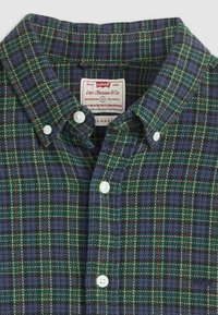 Levi's button-down shirt with green, blue, yellow, and red plaid pattern and white buttons, labeled "Relaxed Fit" and size medium.