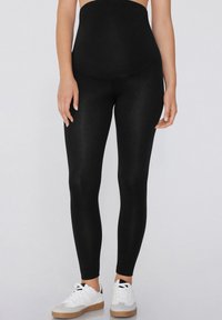 Leggings negros de cintura alta, confeccionados con un material elástico y suave. Llevados con zapatillas blancas que tienen una suela de goma.