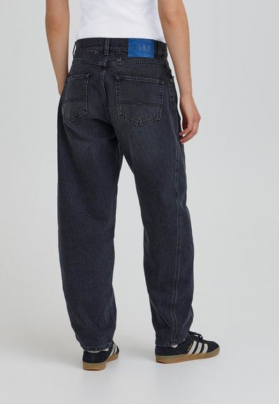 Tumši džinsi ar brīvu piegriezumu, ar zilu etiķeti uz jostas, un divām aizmugures kabatām. Detaļas iekļauj vieglu izbalēšanu un šūšanu.