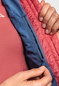 Isolierte Jacke mit roter Außenschicht und blauer Innenseite, ausgestattet mit einer Reißverschlusstasche und strukturiertem Netzstoff, der auf der Innenseite sichtbar ist.