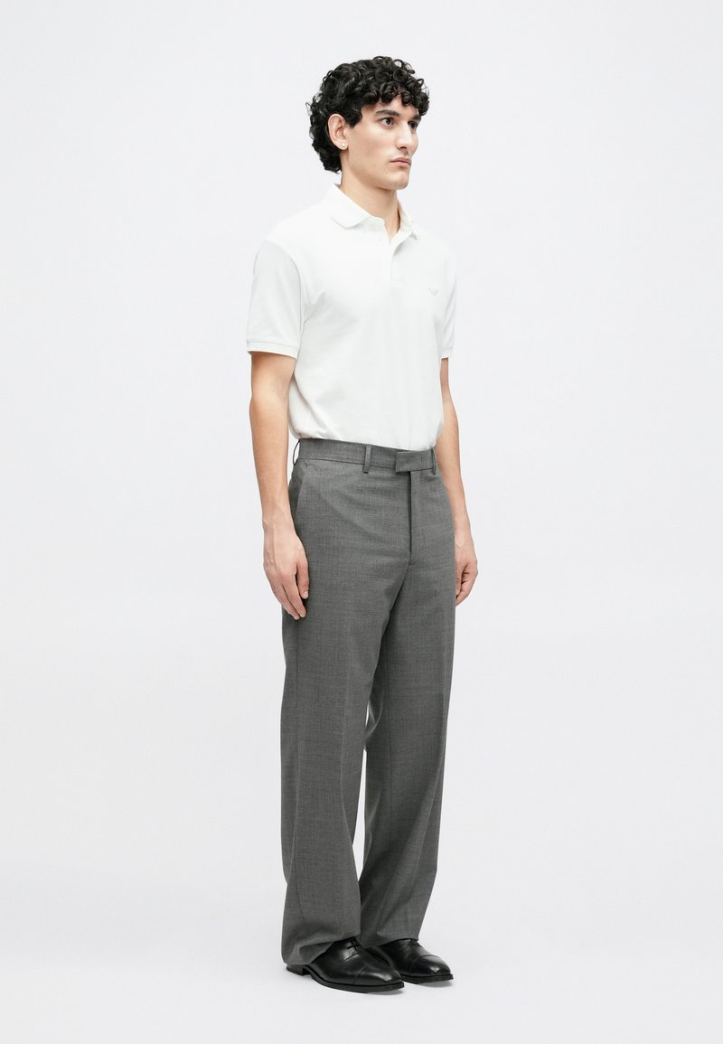 Weißes Polohemd mit kurzen Ärmeln, graue maßgeschneiderte Hose und schwarze Schuhe. Schlichtes Design mit einem dezenten Logo auf dem Hemd.