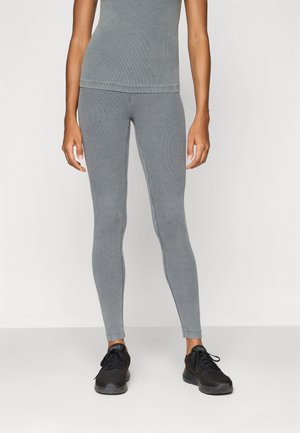 Hallid ribadeta leggings, millel on fitted disain ja elastne materjal, koos mustade spordijalanõudega. Lihtne ja voolav konstruktsioon.