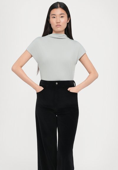 Top scurt de culoare gri deschis cu guler înalt, asortat cu pantaloni largi din bumbac corduroy negri, care au buzunare frontale și un nasture frontal.