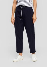Pantalon en coton bleu marine avec taille élastique, poches latérales et jambes fuselées, associé à des sneakers blanches et un haut rayé.