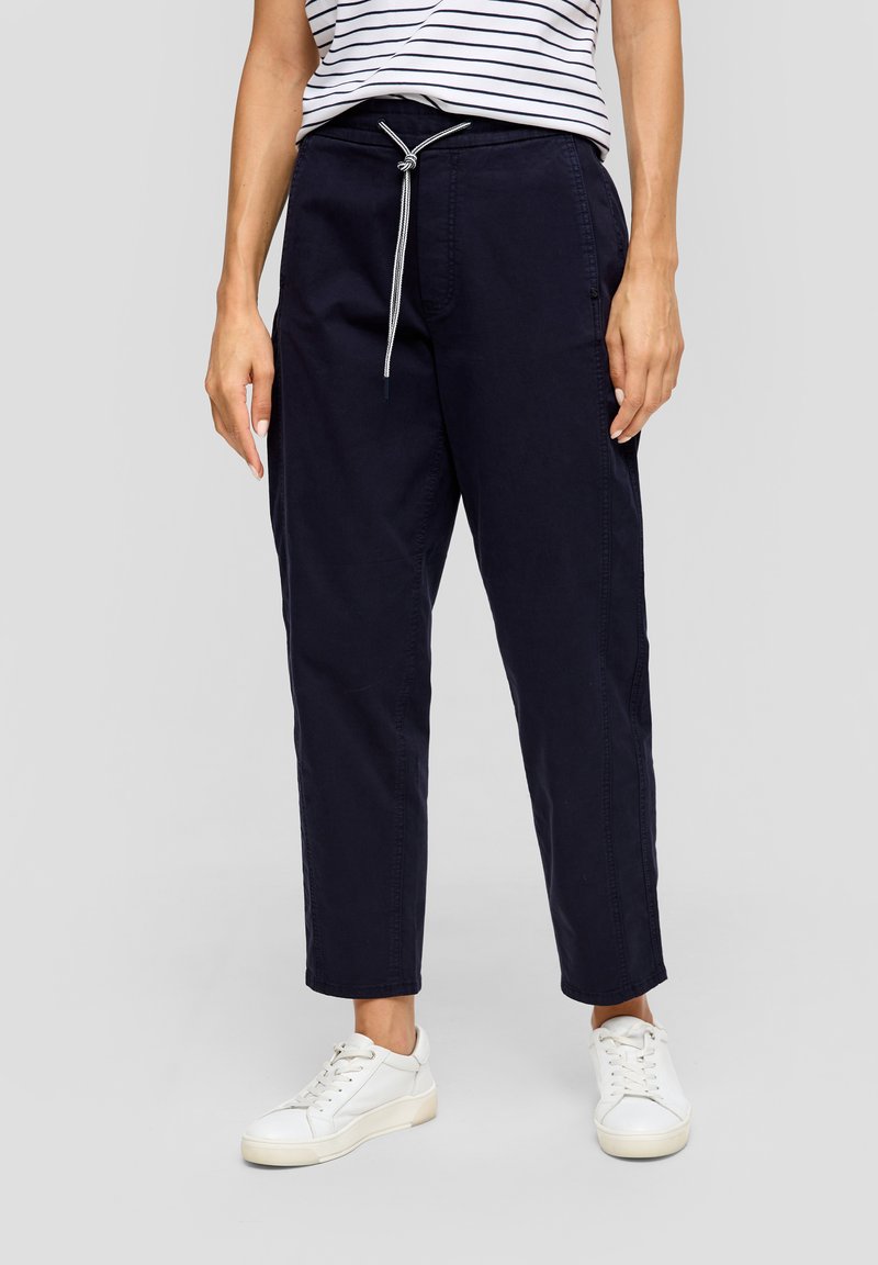 Pantalon en coton bleu marine avec taille élastique, poches latérales et jambes fuselées, associé à des sneakers blanches et un haut rayé.