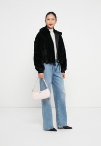 Sort faux fur cropped jakke, grå turtleneck, slidte lyseblå vide bukser, sorte spidse sko og en lys pink håndtaske.