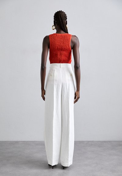 Κόκκινο λαστιχένιο cropped top με φαρδιά λευκά παντελόνια ψηλής μέσης. Λείο υλικό με χαλαρή εφαρμογή, διαθέτει πίσω τσέπες και κομψή σχεδίαση.