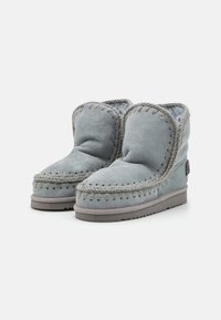 Botas de tobillo de ante gris con costuras visibles, un interior forrado suave y suela de goma plana. Destacan por su diseño de punta redondeada y puño.