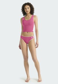 Różowy crop top i zestaw bikini z białymi akcentami. Top ma okrągły dekolt, a dół ma klasyczny krój z logo. Gładka tekstura.