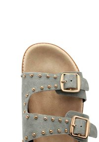Sandalo in suede grigio con due cinturini regolabili, decorato con borchie dorate e una soletta imbottita beige. Include fibbie metalliche per la chiusura.