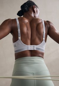Grå trenings-BH med mesh-detaljer, justerbare stropper og krok-lukking. Glatt tekstur, ergonomisk design, i kombinasjon med høyt liv mintgrønne tights.