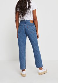 Blå mönstrade jeans med hög midja, rak bendesign och två bakfickor. Kombineras med vita skor och en enkel vit skjorta.