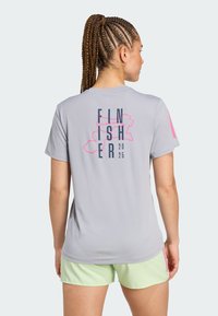 Camiseta deportiva de color gris claro con un gráfico en la parte posterior que dice "FINISHER 2025" en rosa y azul marino. Con mangas cortas; fabricada con tejido que absorbe la humedad.