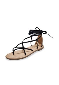 Sandale en cuir noir à lanières avec semelle plate, semelle intérieure beige et détails de couture clairs. Des liens à la cheville complètent le design.