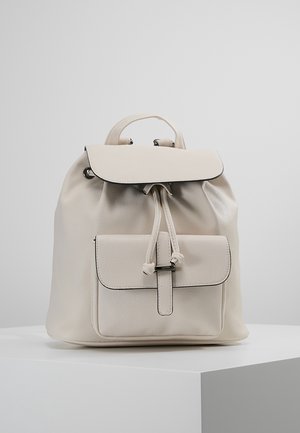 Mochila de cuero crema con cierre de cordón, tapa superior y bolsillo frontal. Presenta un borde negro en contraste y un acabado suave y texturizado.