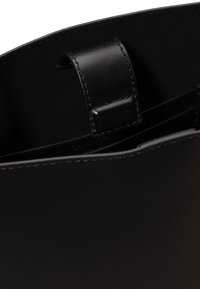 Dettaglio dell'interno di una borsa in pelle nera con anello per tracolla cucito e finitura liscia.