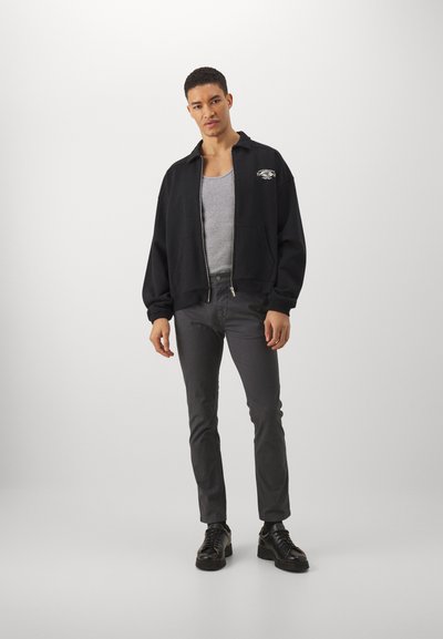 Haut à capuche zippé noir avec poches latérales, débardeur gris, pantalon gris ajusté et chaussures noires. Design simple, style décontracté et matériau léger.