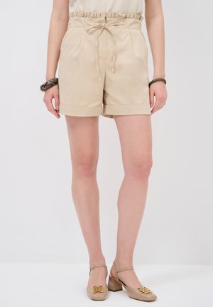 Beige shorts dengan potongan santai, pinggang elastis, dan detail tali serut; tekstur halus dan ker cuffs lipat.