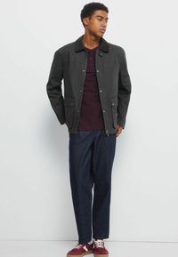 Czarna, lekka kurtka z kołnierzykiem, z przodu na zatrzaski i dwoma bocznymi kieszeniami. Noszona na ciemnoczerwonej koszuli i niebieskich spodniach.