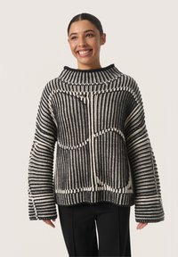 Schwarz-weißer gestreifter Strickpullover mit hohem Kragen, lockerer Passform und weiten Ärmeln, die ein strukturiertes Muster und ein mutiges Design präsentieren.