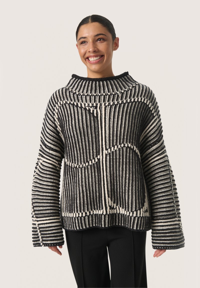 Schwarz-weißer gestreifter Strickpullover mit hohem Kragen, lockerer Passform und weiten Ärmeln, die ein strukturiertes Muster und ein mutiges Design präsentieren.