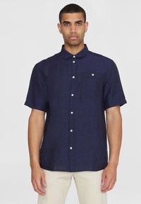 Marinefarbendes, kurzärmliges Hemd aus strukturiertem Leinen mit Kragen, Brusttasche und weißen Knöpfen. Einfaches und klares Design.