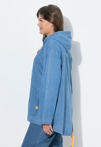 Světle modrá denimová bunda s kapucí, přední kapsou, volným střihem a oranžovým táhlem na spodním lemu. Jemná textura a ležérní design.