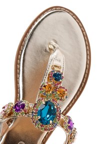 Sándal metálico dorado con acentos de joyas en azul, púrpura y naranja. Presenta un diseño de tiras entre los dedos y una superficie lisa y brillante.