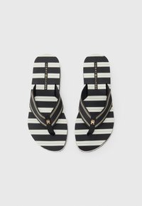 Une paire de tongs rayées noir et blanc de Tommy Hilfiger avec des sangles en tissu noir et des détails de logo dorés sur un fond blanc.